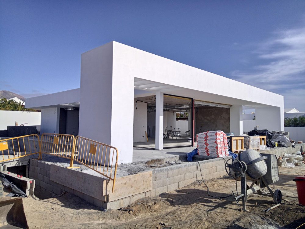 A minimalist white concrete building under construction against a clear blue sky